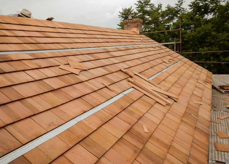The roof of a house is shown as roofers install cedar shingles, shingles, cedar shingles, cedar shake shingles, cedar shake, roof, roofing, roofer, cedar roof, trees, sky, workers, house, housetop