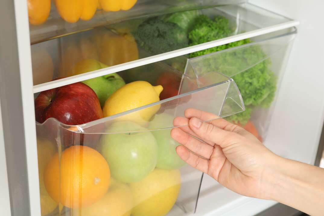 Woman opening refrigerator drawer with fresh fruits, closeup