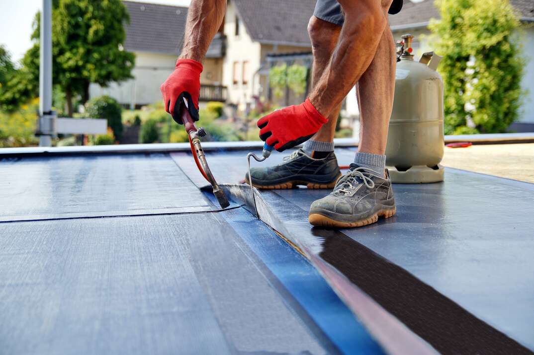 Flat roof installation with propane blowtorch during construction works with roofing felt. Heating and melting bitumen roofing felt.