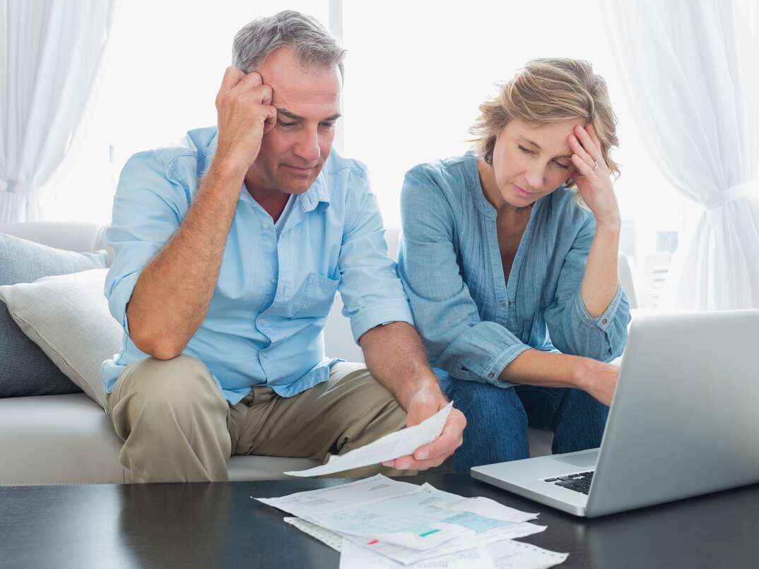 Worried couple paying their bills online with laptop at home in the living room