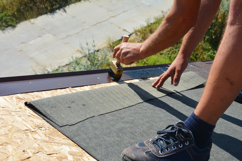 A building contractor is installing underlayment, a layer of bitumen tape on sheathing for overall roof protection at the ridge of the rooftop on the house construction, repairing.