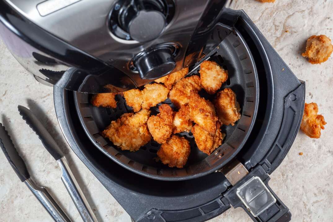 A stainless steel air fryer is shown with its cooking compartment open and full of chicken wings while a pair of kitchen tons sits next to the fryer on the table, air fryer, chicken wings, appliances, fryer, kitchen appliances, tongs, cooking, chicken, wings, food