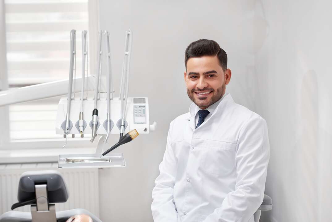 Young cheerful male professional dentist smiling to the camera joyfully sitting at his office copyspace dental oral examination checkup professionalism occupation medicine doctor.