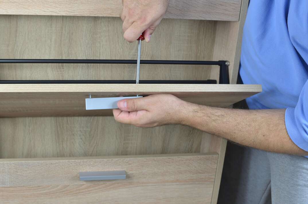 Fixing a pull on a drawer of a shoe cabinet with a screwdriver