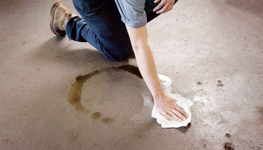 Oil clean-up in a workshop. A man cleaning-up an oil spill on a workshop floor.  The man is wearing work boots and mechanic's clothing.