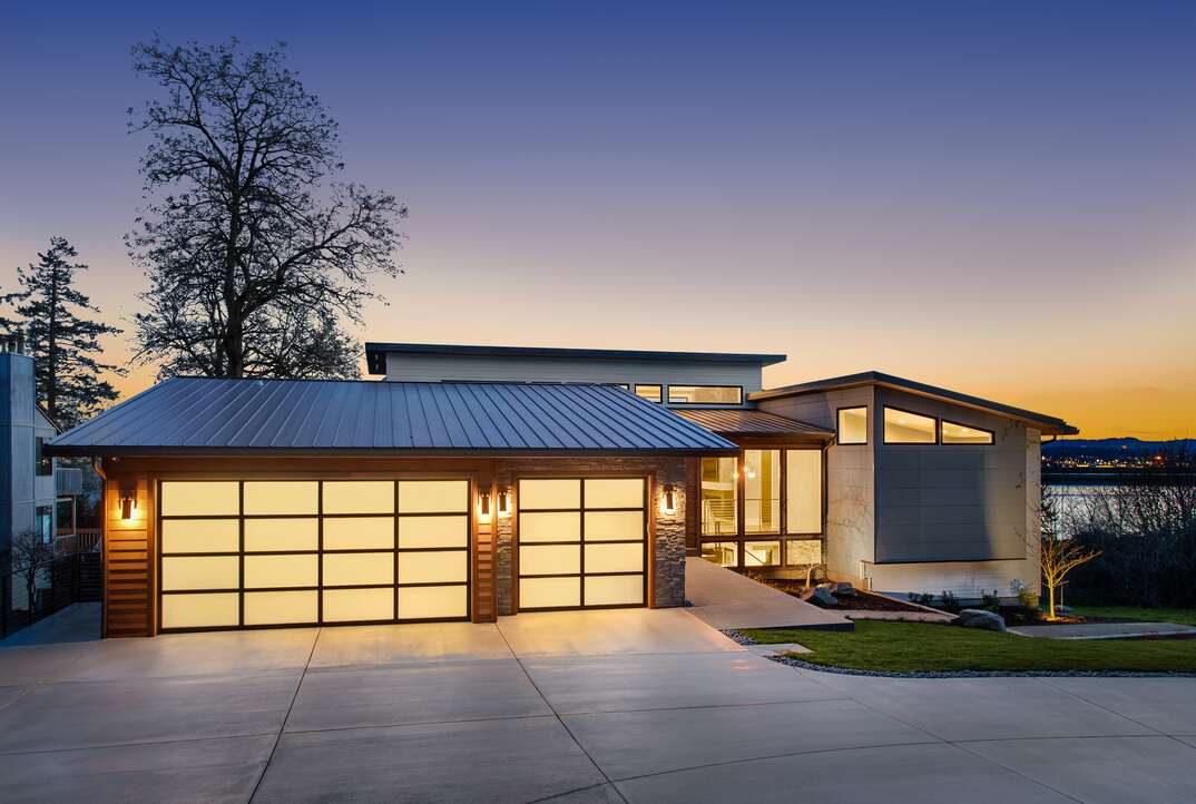 A beautiful sunset behind a modern hose with a glass garage door and a concrete driveway