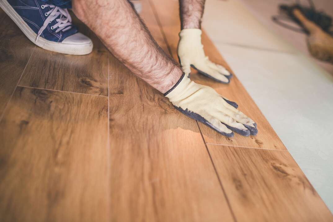 close up of a man wearing work gloves assembling bamboo floor boards with tongue and groove cuts 