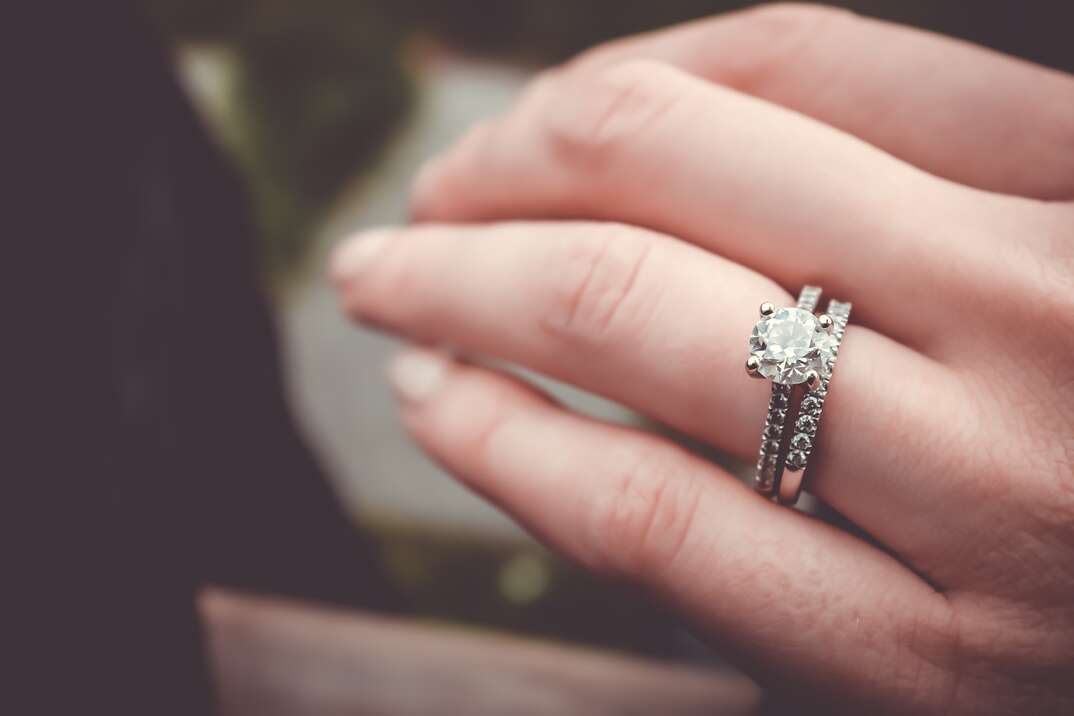 A closeup of a female hand shows her four fingers and a diamond engagement ring with a wedding band on the ring finger, wedding ring, ring, wedding, engagement ring, engagement, engaged, fiancee, fiance, diamond, diamond ring, fingers, female fingers, woman, woman's hand, woman's fingers, ring finger, wedding band, jewel, jewelry