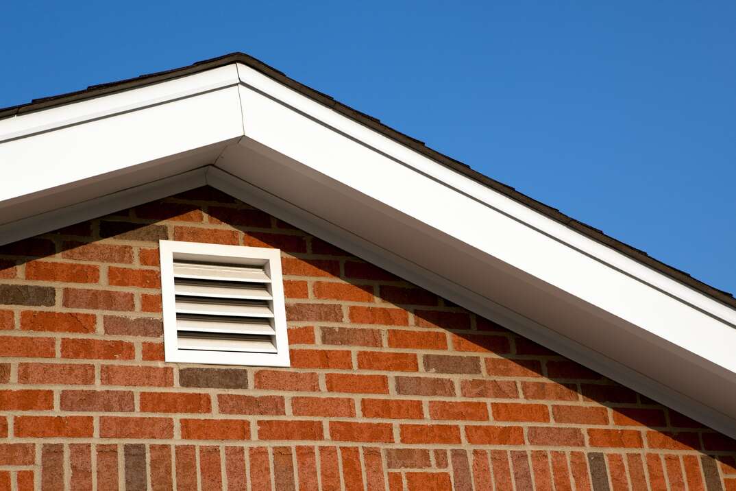 a white gable vent sits under a roof overhand on a brick home