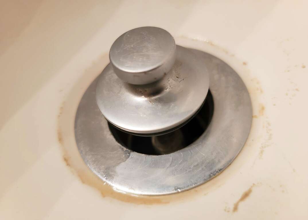 A dirty bathtub drain sits in the open position